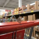 A close-up of a quarter being inserted into an Aldi shopping cart handle in a grocery store aisle.