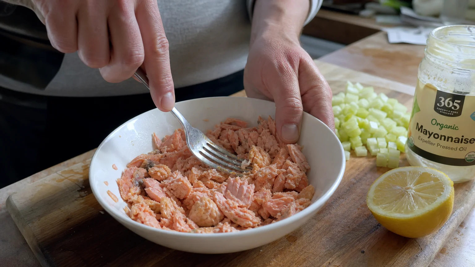 A person flaking canned wild-caught salmon in a white bowl with a fork, preparing a high-protein meal.