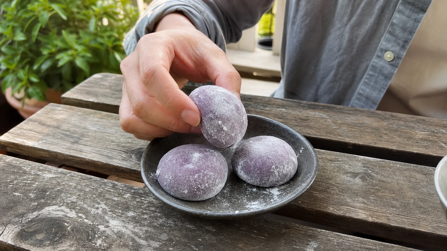 Candid photo of a hand picking up a purple ube mochi ice cream ball from a ceramic plate.