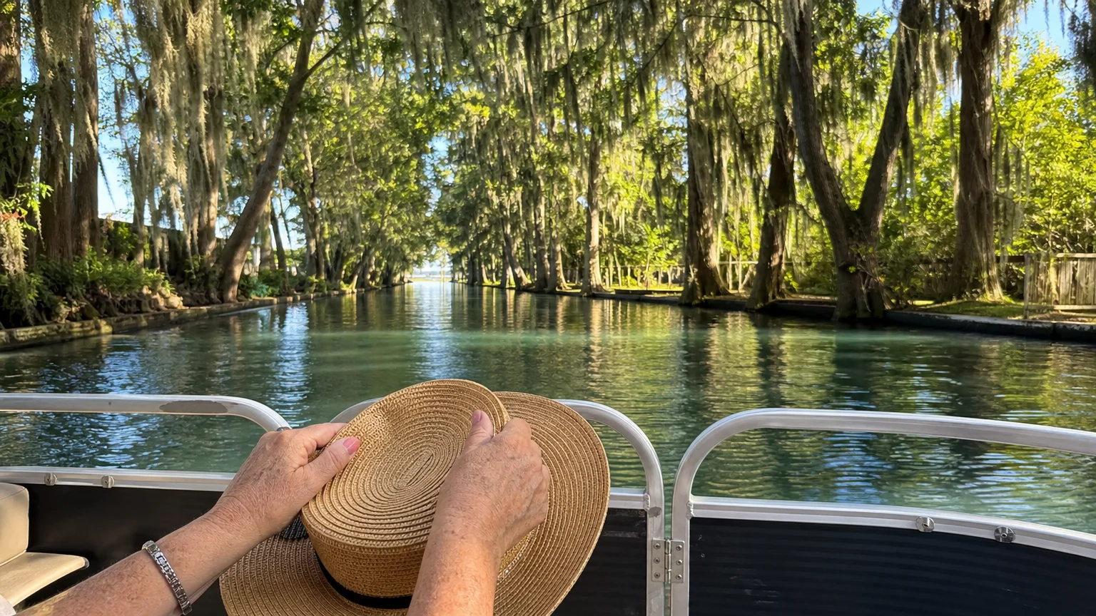 View from a pontoon boat traveling through a tree-lined canal connecting lakes in Winter Haven, Florida.